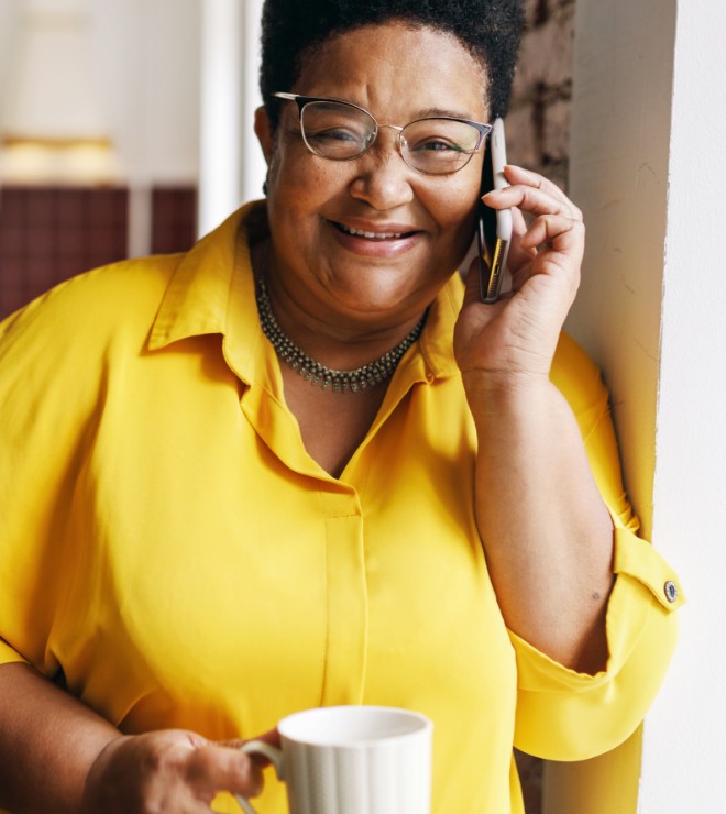 Lady talking on her phone holding a cup of tea and wearing a bright yellow shirt